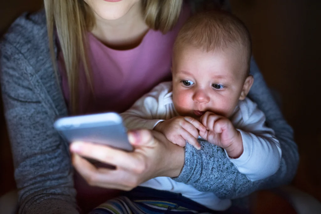 This image shows a picture of a mom holding her baby while text messaging with her mobile phone